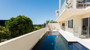 A modern house with a swimming pool, a balcony with a view of the greenery, and a large sliding glass door. - Indulge at Iluka, Castaways Beach (Noosa)