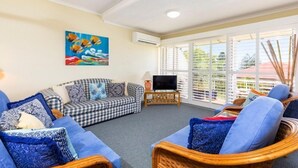A living room with a checkered sofa, blue cushions, a television on a wooden stand, and a painting on the wall. - Bright & comfortable, Sunshine Beach (Noosa)