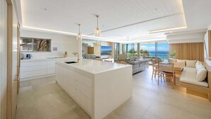 Eine moderne Küche mit einer großen Kochinsel, ein Essbereich mit Aussicht und ein Wohnbereich mit Sofa und Tisch.