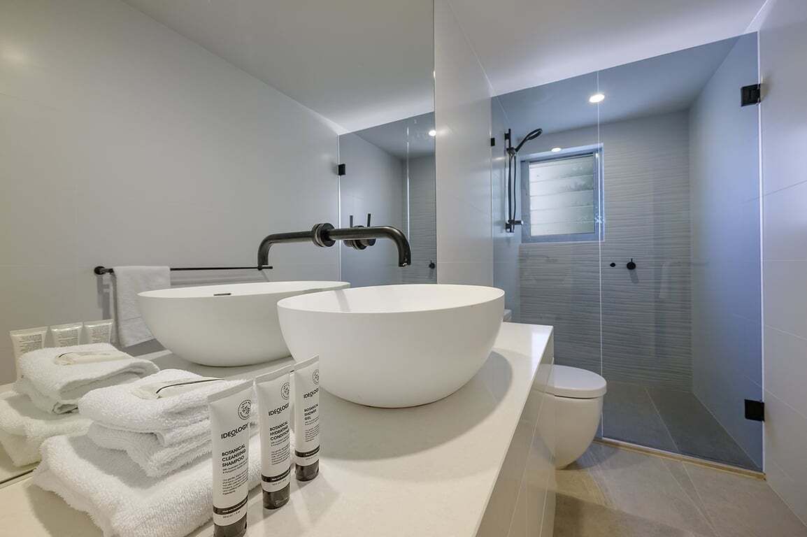 Une salle de bain moderne avec deux grands lavabos blancs, des toilettes et une douche à parois de verre.