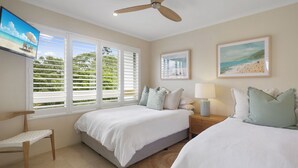A bedroom with two beds, a ceiling fan, a TV, and artwork on the walls.