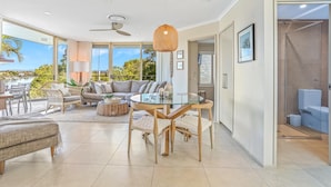 A spacious living area with a glass dining table, comfortable seating, and a view of the outdoors.