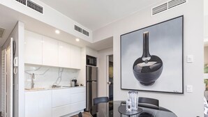 A modern kitchen with white cabinets, a stainless steel refrigerator, and a glass dining table with black chairs. - Modern & quiet on Hastings Street (Noosa Heads)