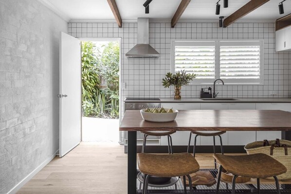 Una cocina moderna con una isla de madera, dos taburetes de bar, un cuenco de fruta y una ventana con persianas.