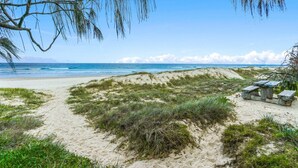A beach with a sandy path, some grass, and a bench area.