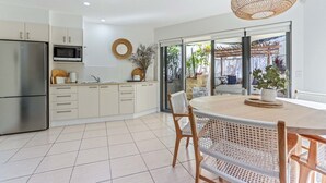 A modern kitchen with a built-in microwave, stainless steel refrigerator, and a dining area with a round table and wicker chairs.