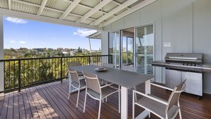 A covered outdoor area with a table and chairs, a grill, and a view of the surrounding landscape.