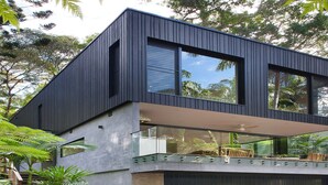 Ein modernes, zweistöckiges Haus mit dunkler Fassade, großen Fenstern und einem überdachten Außenbereich mit Treppen, die zur Garage führen.