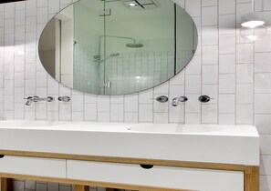 Ein Badezimmer mit weißem Waschtisch, einem runden Spiegel und einer Duschkabine.