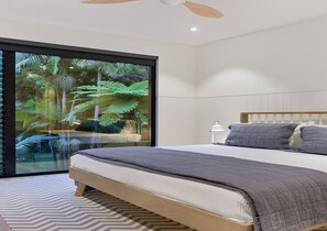 Ein modernes Schlafzimmer mit einem großen Bett, einem Deckenventilator und Blick auf einen tropischen Wald durch eine Schiebeglastür.
