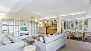A modern living room with a grey sofa, a TV, and a dining area with a wooden table and chairs. - Retreat to tranquillity, Noosa Heads (Noosa Heads)