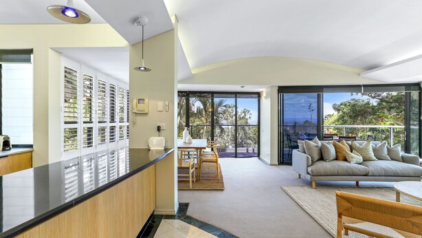 A modern living room with a sofa, a dining area, and a kitchen with a counter. - Retreat to tranquillity, Noosa Heads (Noosa Heads)
