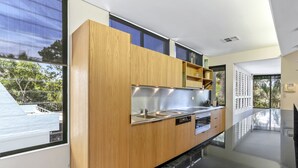A modern kitchen with wooden cabinets, stainless steel appliances, and a large window offering a view of the outdoors. - Retreat to tranquillity, Noosa Heads (Noosa Heads)