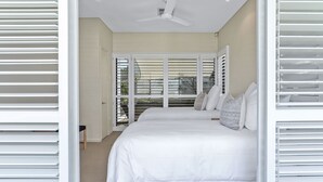 A bedroom with a large bed, white blinds, a ceiling fan, and a view through the window. - Retreat to tranquillity, Noosa Heads (Noosa Heads)