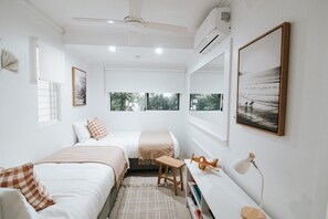 Two single beds with matching bedding, a bedside table, and a small bench in a serene room with a view.