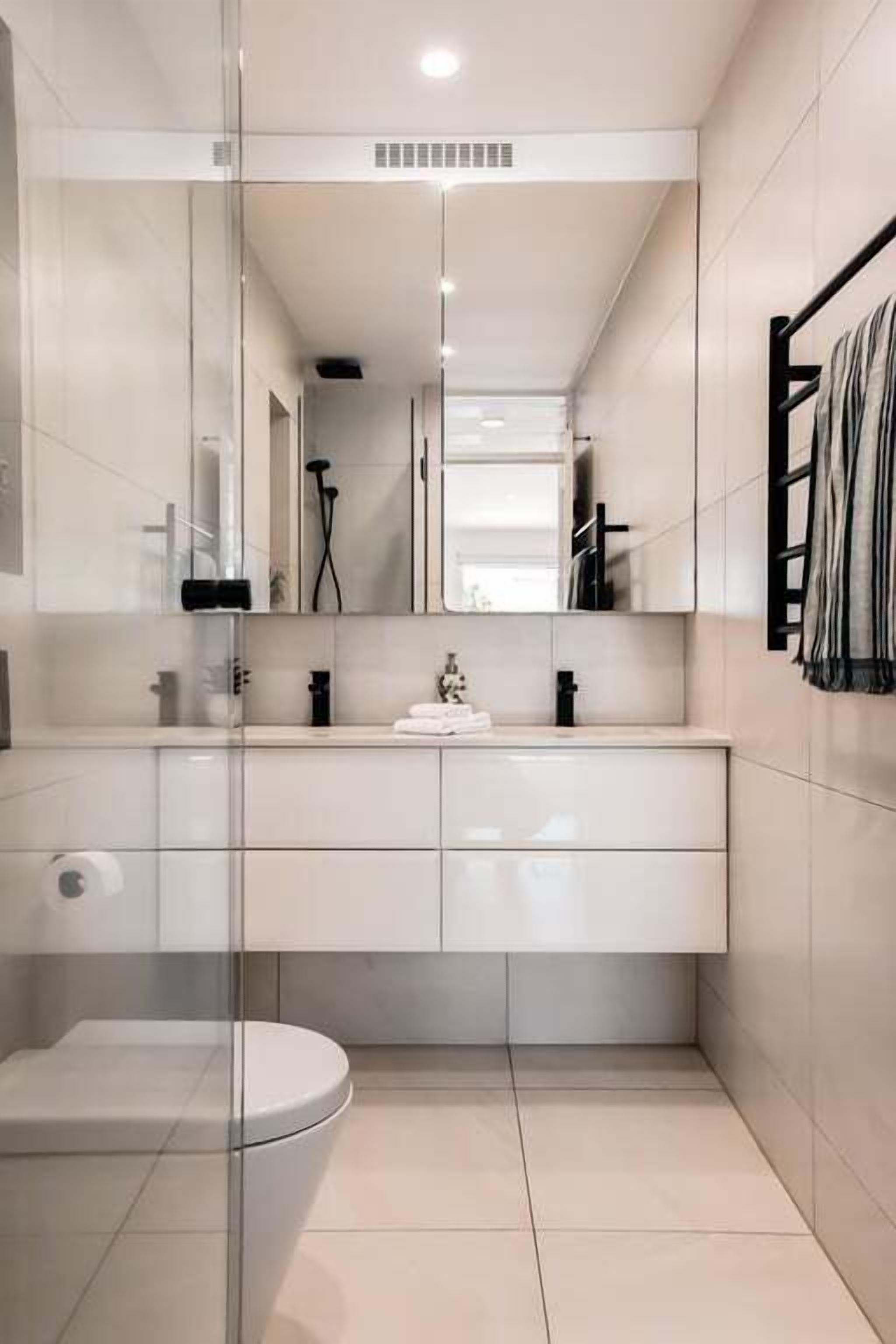 A modern bathroom with a glass partition, a white toilet, a vanity with a mirror, and a towel rack.