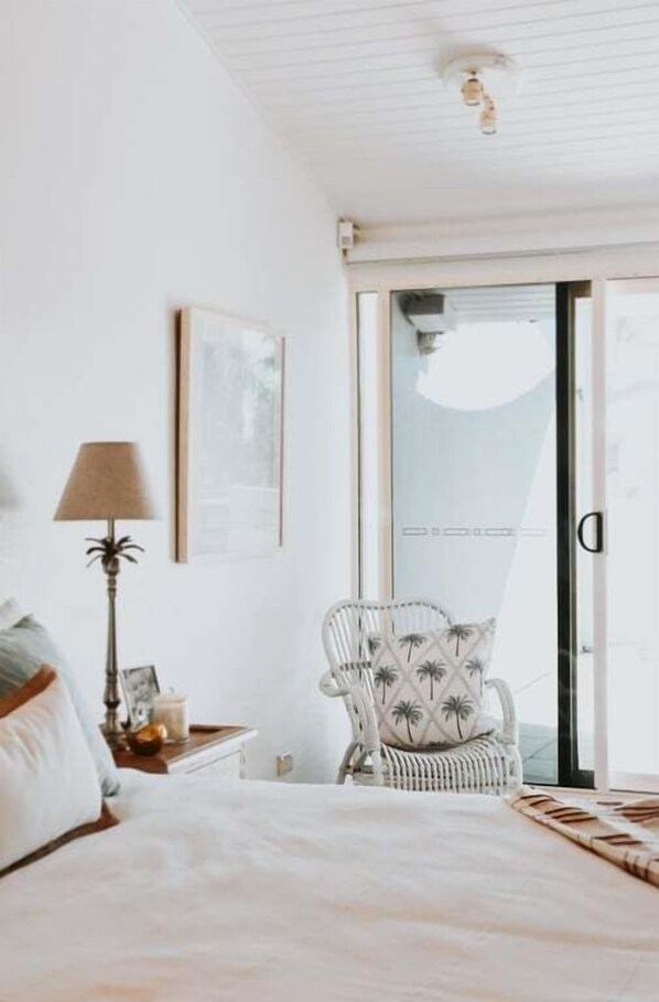 Une chambre à coucher comprenant un lit, une table de chevet, une lampe, une chaise et une porte-fenêtre coulissante donnant sur un balcon.