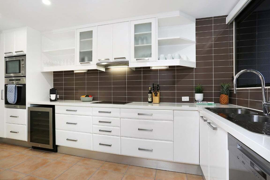 A modern kitchen with white cabinetry, a built-in oven, a dishwasher, and a stainless steel sink.