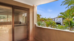 A balcony with a sliding door, a tiled floor, and a view of palm trees and buildings. - Riverside location, Noosa Sound (Noosa Heads)