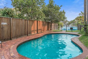 Relax by the pool surrounded by lush greenery and a brick walkway.