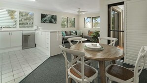 A modern kitchen with white cabinets, a dining area with a round wooden table, and a gray sofa. - Riverside location, Noosa Sound (Noosa Heads)