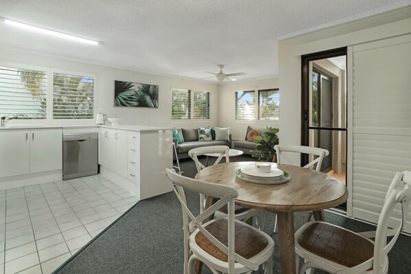A modern kitchen with white cabinets, a dining area with a round wooden table, and a gray sofa.