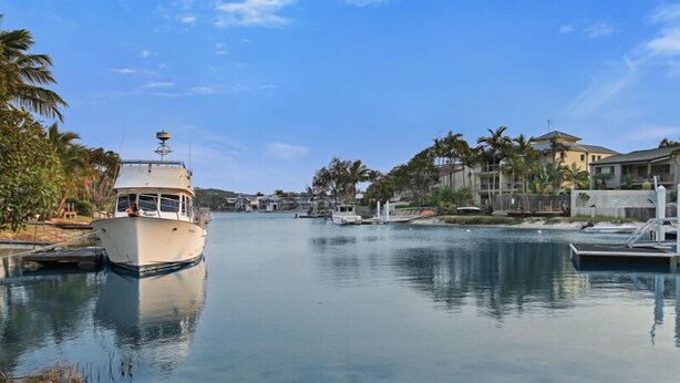 A boat docked at a marina with a calm water body, surrounded by residential buildings and palm trees. - Riverside location, Noosa Sound (Noosa Heads)