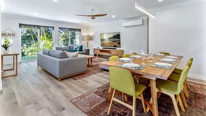 Una sala moderna con un sofá gris, una mesa de comedor dispuesta para seis personas y un ventanal con vistas a zonas verdes.