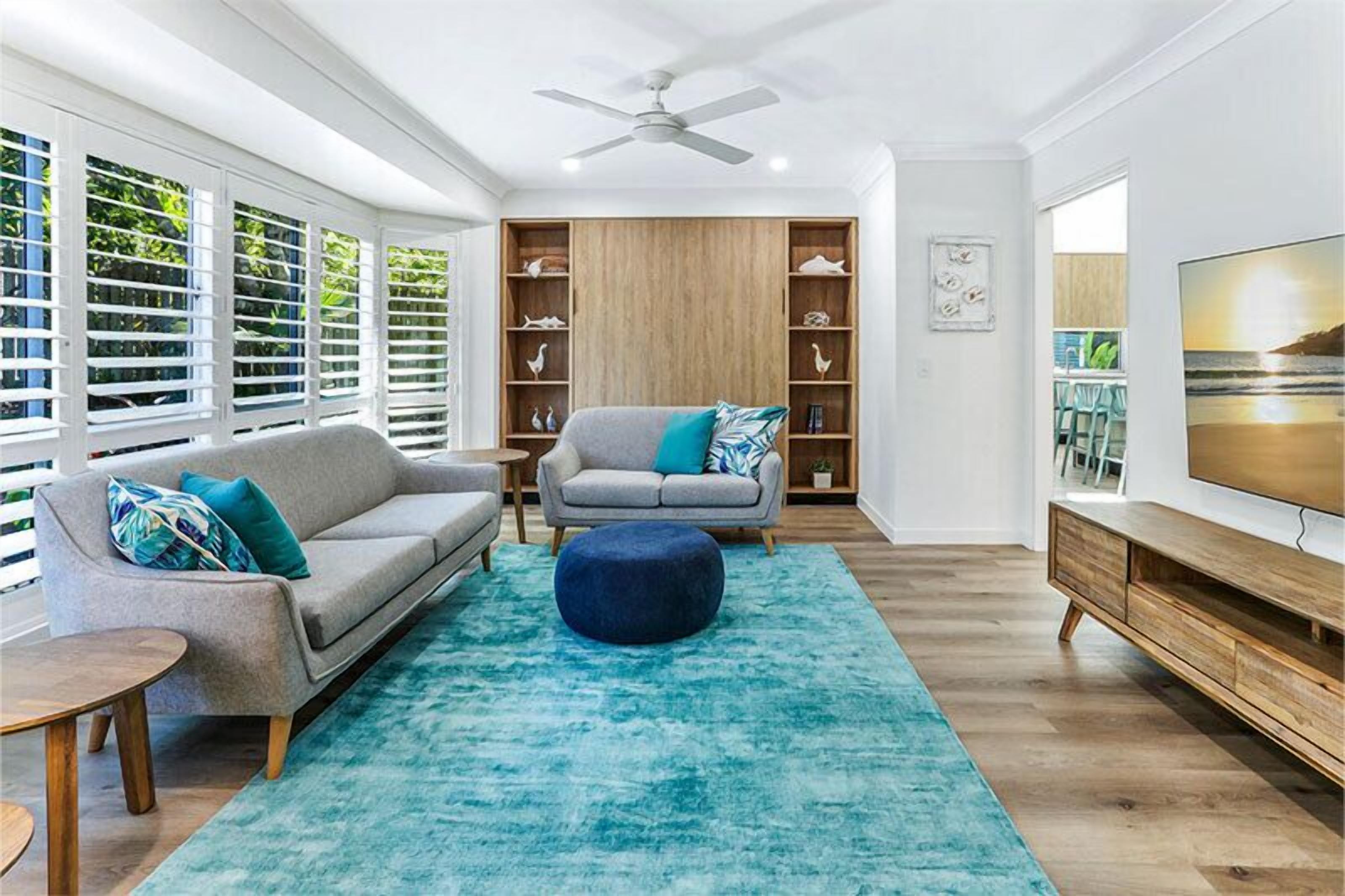 Ein modernes Wohnzimmer mit grauem Sofa, blauem Ottomanen und einem Holzschrank.