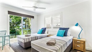 Un dormitorio con dos camas, un ventilador de techo, una mesita de noche con lámpara y vistas a zonas verdes.