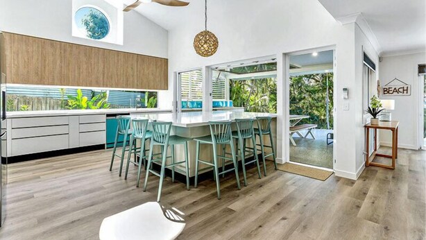 Una cocina moderna con una isla central, sillas color turquesa y un ventilador de techo.