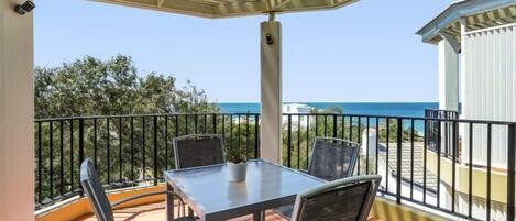 A balcony with a table and chairs, overlooking a coastal view.