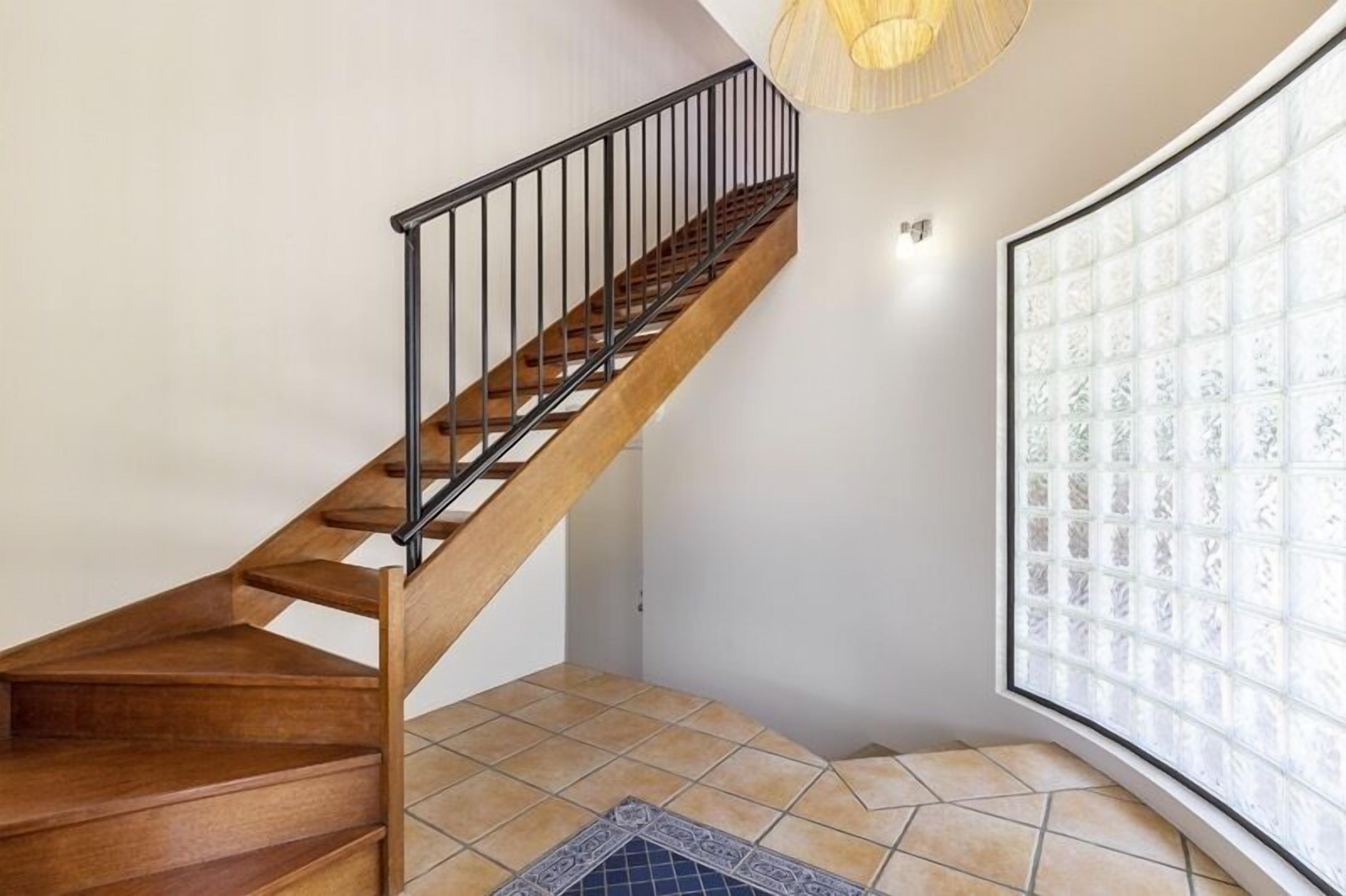 A wooden staircase with a black railing, leading to a room with a large window and patterned glass.