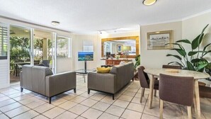 Ein Wohnzimmer mit einer Couch, einem Esstisch mit Stühlen und Blick ins Freie durch große Fenster.
