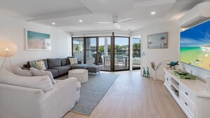 A modern living room with a grey sectional sofa, a round coffee table, and a large flat-screen TV. - Peaceful riverside living in Noosa Heads (Noosa Heads)