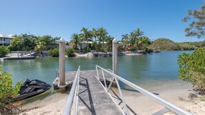 A marina with a concrete dock leading into calm waters, surrounded by palm trees and a clear sky. - Peaceful riverside living in Noosa Heads (Noosa Heads)
