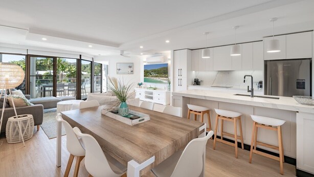 A modern kitchen with white cabinets, a stainless steel refrigerator, and a large island with stools. - Peaceful riverside living in Noosa Heads (Noosa Heads)