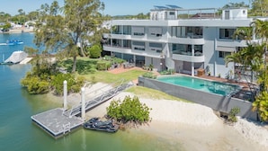 A modern multi-story building with a pool, surrounded by greenery and a dock. - Peaceful riverside living in Noosa Heads (Noosa Heads)