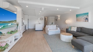 A modern living room with a large TV, a sofa, a dining area, and a kitchen. - Peaceful riverside living in Noosa Heads (Noosa Heads)