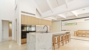 A modern kitchen with a marble island, wooden cabinets, and a dining area with bar stools.