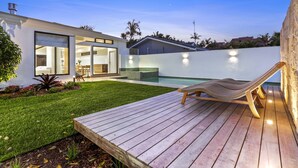 A modern house with a swimming pool, a wooden deck, and a lounge chair.