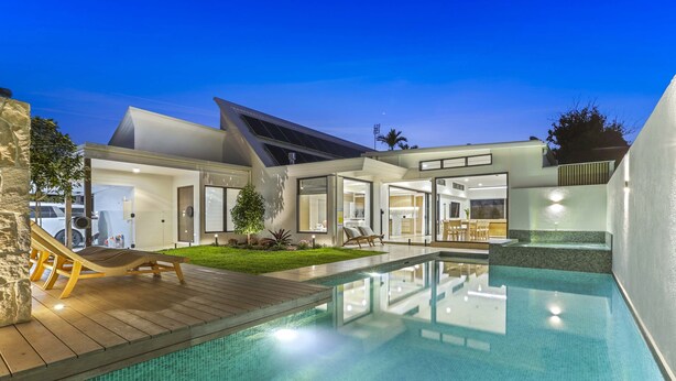 A modern house with a swimming pool, a patio with lounge chairs, and a well-maintained garden.