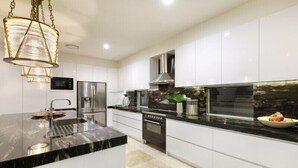 Une cuisine moderne avec des meubles blancs, un plan de travail en marbre noir, des appareils en acier inoxydable et un luminaire suspendu.