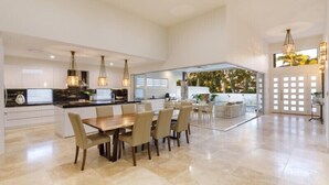 Une cuisine spacieuse avec un coin repas, des luminaires suspendus modernes et une grande fenêtre donnant sur un jardin.