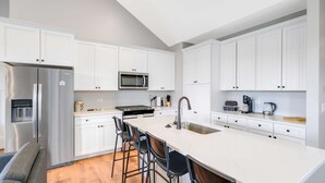 Een moderne keuken met witte kasten, een roestvrijstalen koelkast, een magnetron, een fornuis en een groot eiland met barkrukken.