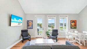 Een woonkamer met uitzicht op een strand, twee fauteuils, een bijzettafeltje en een eethoek met witte meubels.
