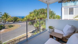 Un balcon avec vue sur l’océan, une balustrade blanche et un espace détente avec des coussins.