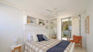 Une chambre à coucher avec un lit, une chaise, un ventilateur de plafond et une fenêtre avec des rideaux.