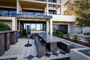 CHALET & CO. features a modern entrance with a glass door and a welcoming seating area amidst a beautifully landscaped garden.