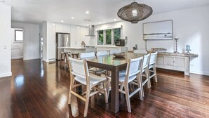 A spacious kitchen with a large island, wooden chairs, and a hanging light fixture.